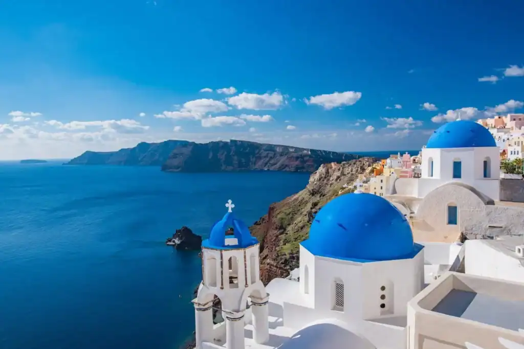 Iconic blue-domed churches of Oia overlooking the Aegean Sea and caldera cliffs in Santorini, Greece.