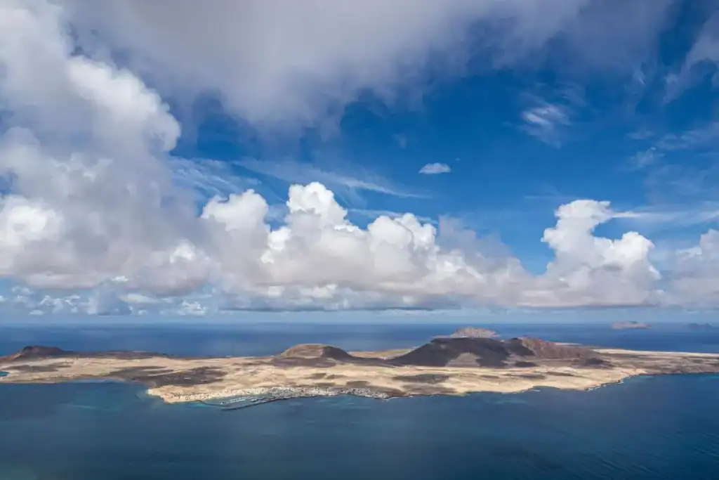 unknown islands in Europe. Aerial view of La Graciosa island from Mirador Del Río, showing volcanic terrain, clear blue ocean, and dramatic clouds over the Canary Islands.