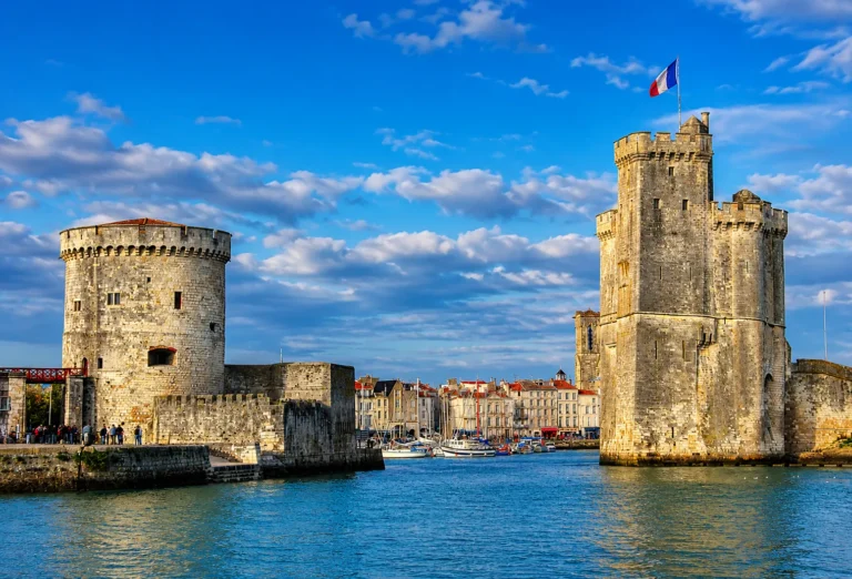 The historic medieval stone towers guarding the sunny Old Port of La Rochelle in France, with blue water in the foreground.