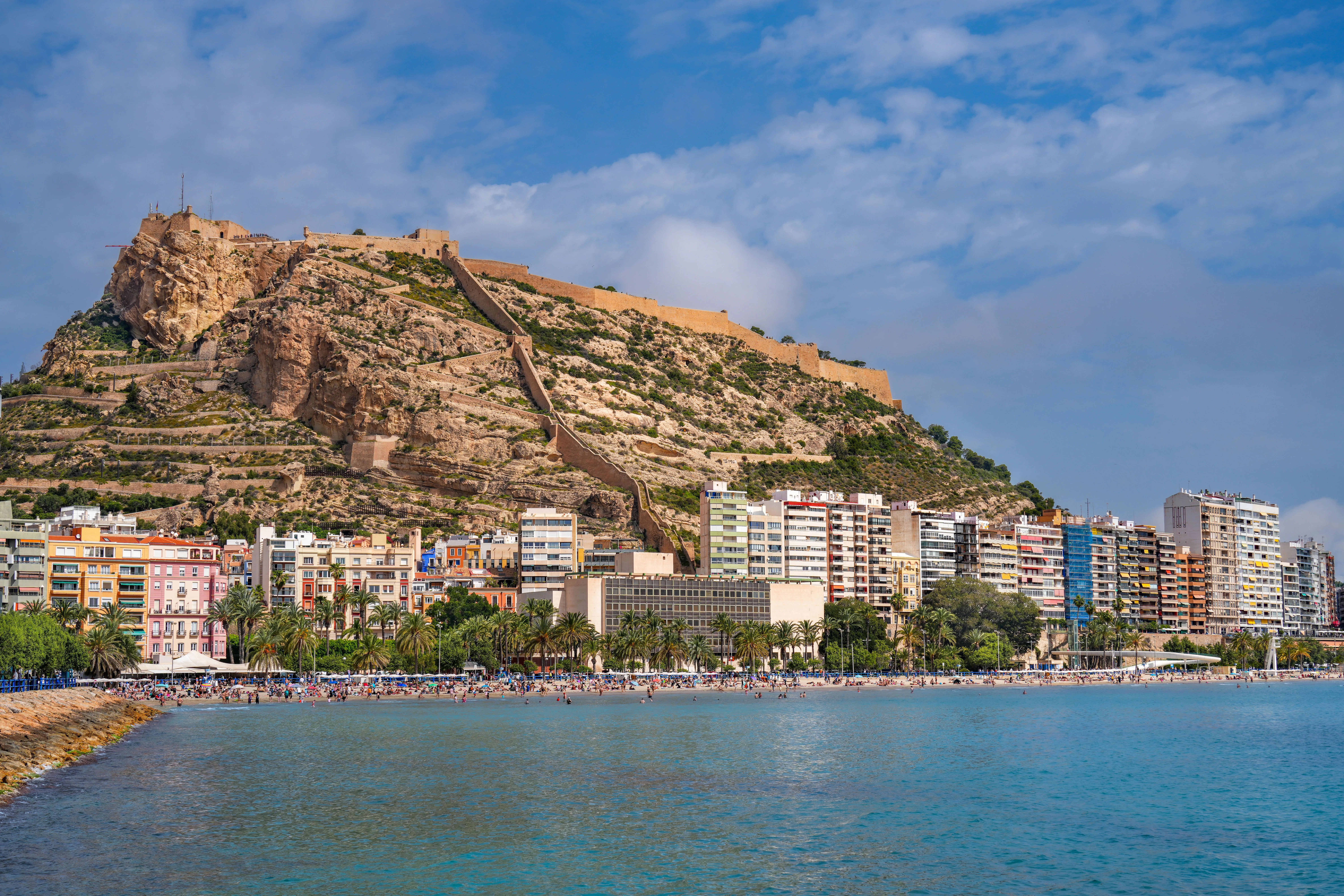 Scenic view of Postiguet Beach and the Mediterranean coastline with Castillo de Santa Bárbara perched atop Mount Benacantil in Alicante, Spain.